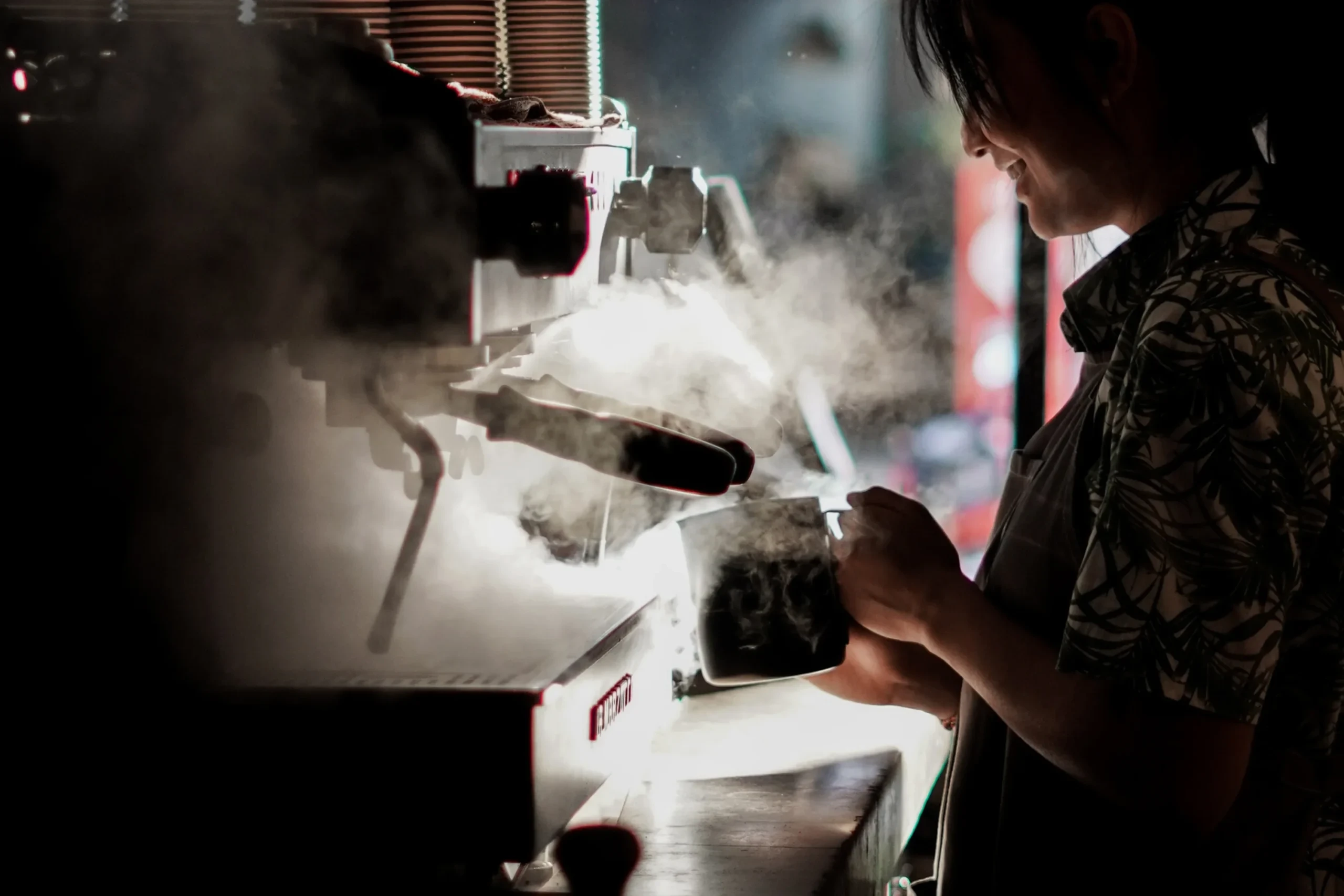 Gemini said A smiling barista steaming milk with a professional espresso machine, surrounded by a thick cloud of white steam in a moody cafe setting.