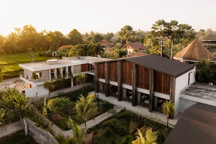 An aerial view of the Syrco BASE restaurant and bar complex in Ubud, featuring modern wooden and white architecture surrounded by lush tropical greenery and gardens at sunset.