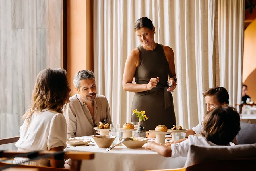 A family enjoying a fine dining experience at Syrco BASE Restaurant and Bar, featuring elegant table settings and attentive service in a brightly lit, modern interior.