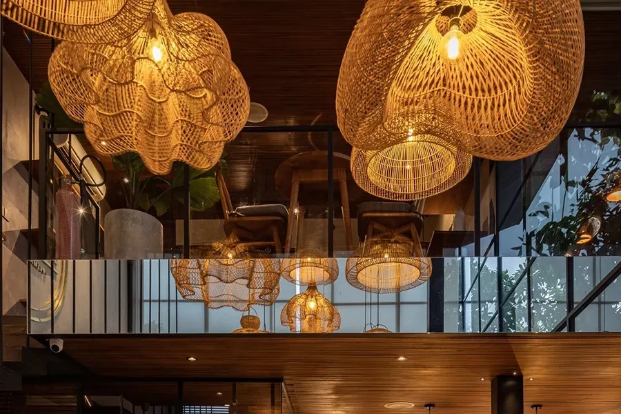 Large, ornate woven wicker pendant lights hanging from a dark wooden ceiling in a two-story modern building with glass railings and warm ambient light.