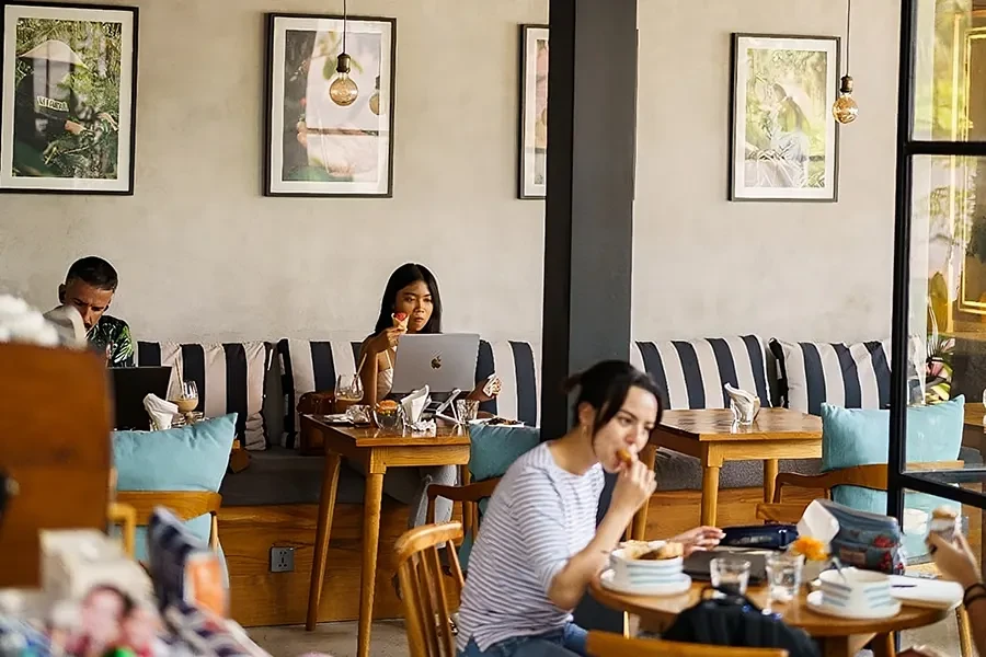Warm modern interior of Bali Beans Coffee featuring a marble service counter, professional espresso machine, and wooden seating area with striped cushions.
