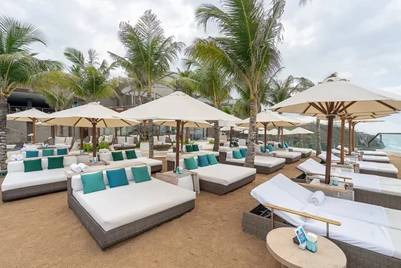 Tropical outdoor seating area with white daybeds and palm trees at Oneeighty Bali.