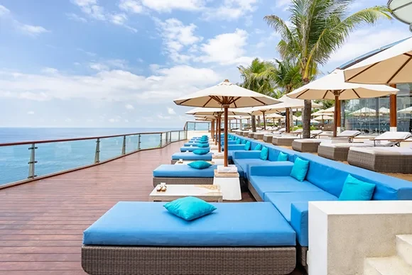 Rows of blue daybeds and white umbrellas on the wooden deck at Oneeighty cliff club.