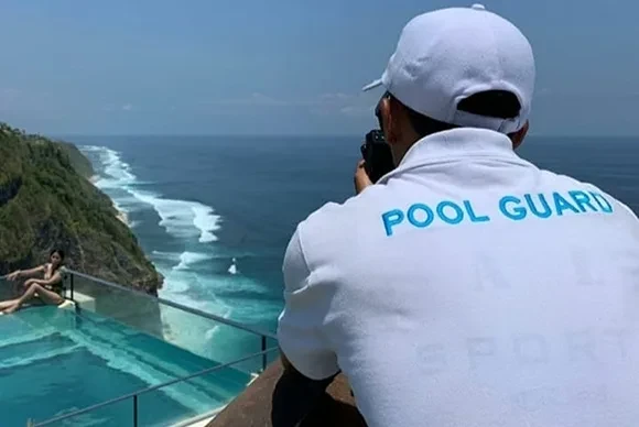 A Oneeighty pool guard taking a photo of a guest in the glass-bottom sky pool overlooking the Uluwatu cliffs.