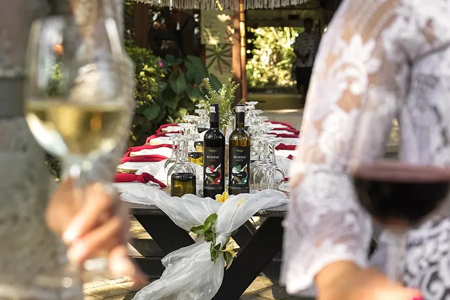 An elegant outdoor long-table dining setup at House of Sababay, featuring Sababay Reserve Red and White wine bottles as centerpieces with white lace decor and guests enjoying wine.
