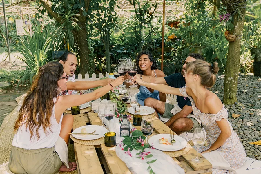 A romantic garden picnic experience at House of Sababay Bali, featuring a couple sharing snacks at a decorated outdoor table with premium wine glasses and floral arrangements.