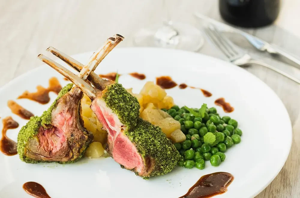 Herb-crusted lamb chops served with minted peas and roasted potatoes, perfectly paired with a glass of Hatten Wines' premium Bali-grown red wine.