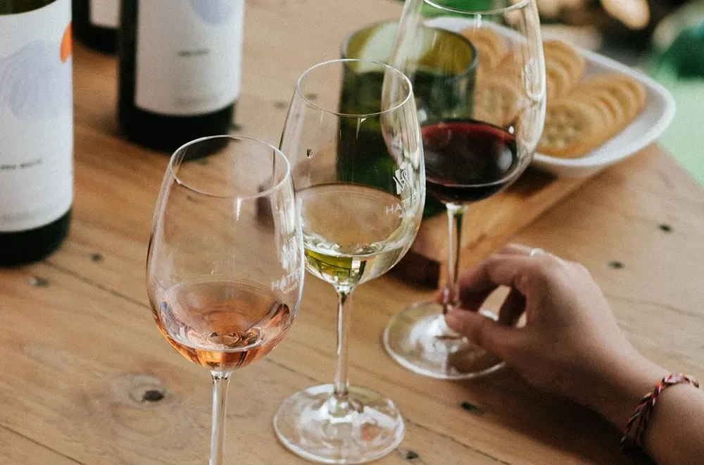 A flight of Hatten Wines including Rosé, White, and Red varieties served on a wooden tasting table with crackers at a Bali vineyard.